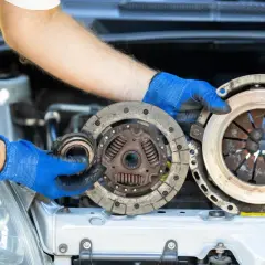 Mechanik w niebieskich rękawiczkach pokazuje zużyte części sprzęgła. Zastanawiasz się, ile kosztuje wymiana sprzęgła?