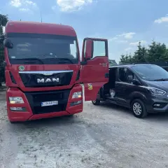 Czerwona ciężarówka MAN z otwartymi drzwiami obok ciemnego vana Ford.