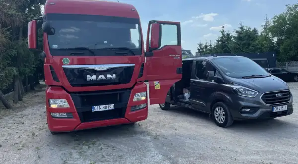 Czerwona ciężarówka MAN z otwartymi drzwiami obok ciemnego vana Ford.